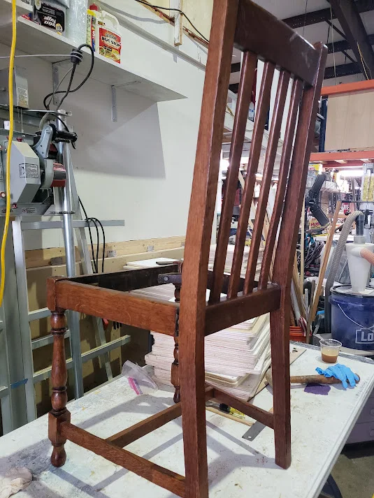 The wooden frame of the chair sits on a workbench with the upholstered seat removed for structural assessment.