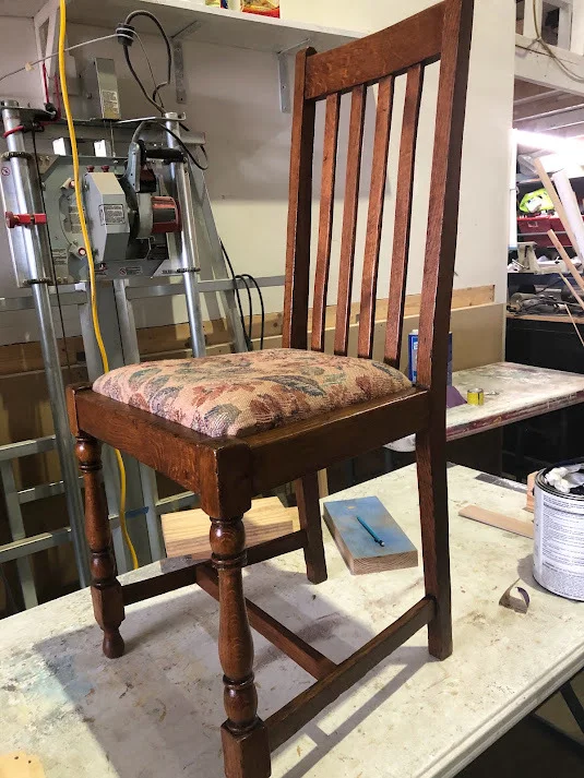 A fully restored century-old wooden chair with a patterned fabric seat standing on a workshop table.