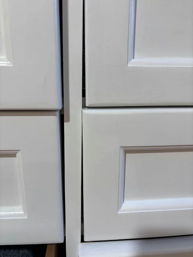 Close-up of misaligned white drawer fronts with uneven gaps due to a sagging frame.