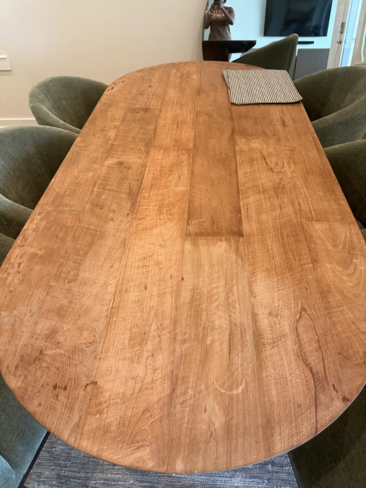 A close-up of an unsealed wood dining table showing light liquid stains, ring marks, and food spots.